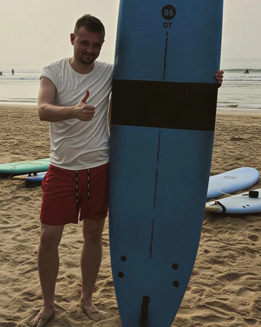 Rafał Nowak, właściciel withplus.pl, na plaży z deską surfingową